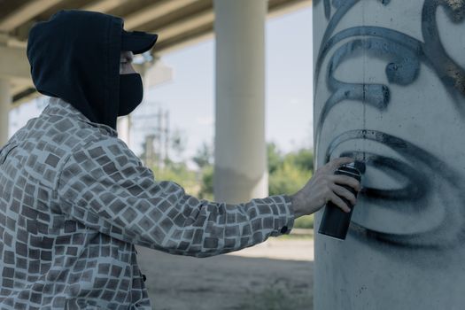 Artiste de street art peignant un mur sous un pont avec une bombe de peinture, ambiance urbaine et créative.